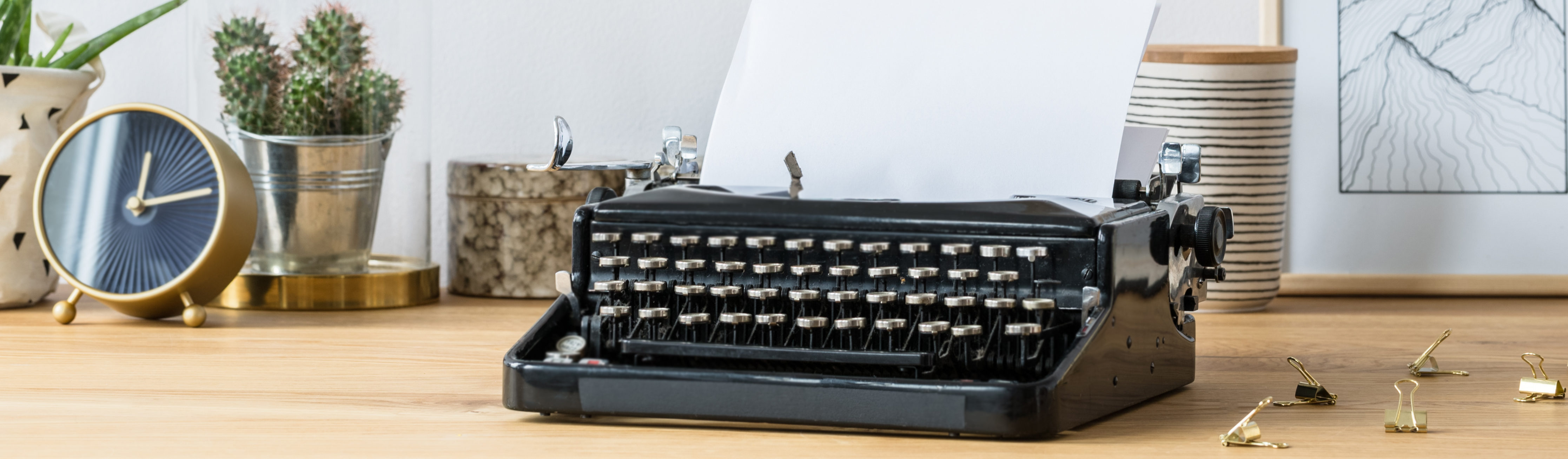 Vintage typewriter standing on a wooden home office desk with fresh plants, handmade poster and decorations